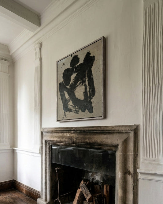 Vintage fireplace with a framed abstract painting above it in a room with wooden flooring.