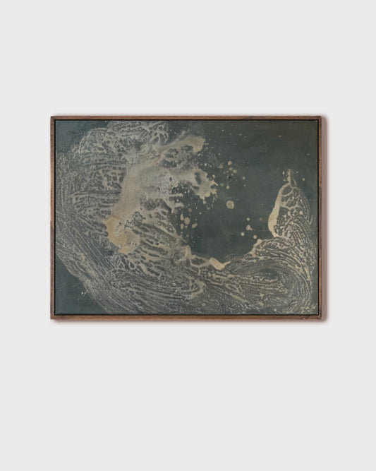 A framed abstract art print featuring textured organic patterns in dark gray, beige, and gold tones, set against a solid light gray background.