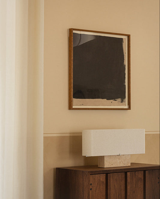 Framed abstract painting on a beige wall above a wooden cabinet with a lamp.