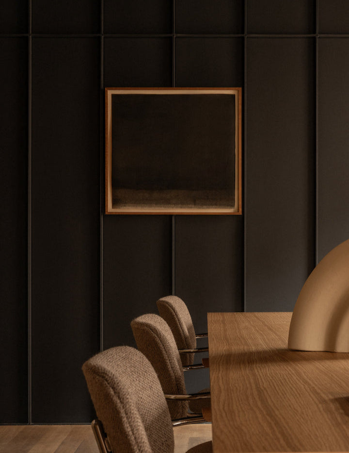 Dining area with wooden table and chairs against a dark paneled wall.