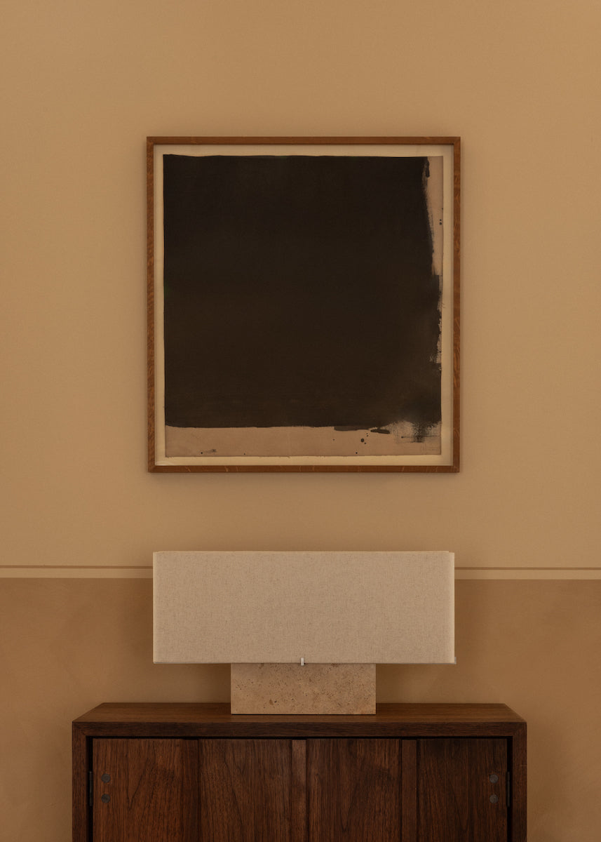 Framed abstract painting on a beige wall with a wooden sideboard below.