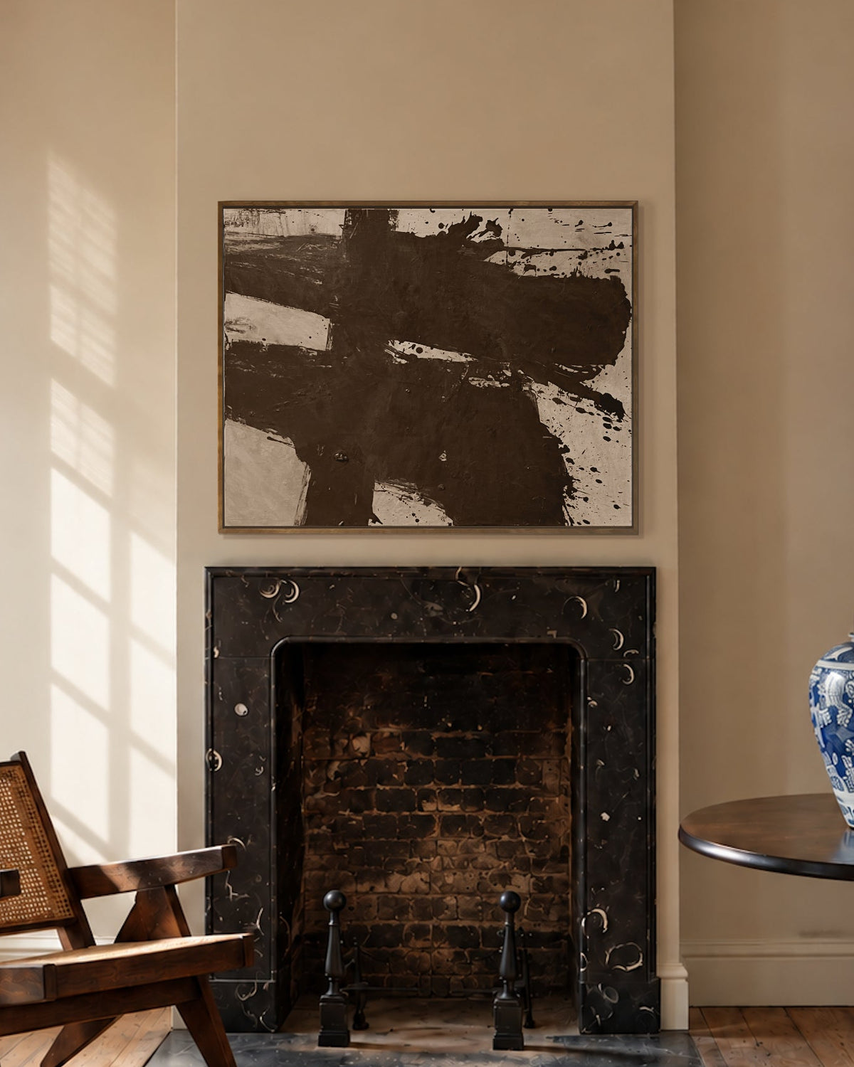 A Makelberge styled interior room with a black marble fireplace, a large abstract painting above it, a wooden armchair by a window, a round black side table with a blue-and-white ceramic vase, and a woven rug on a wood floor.