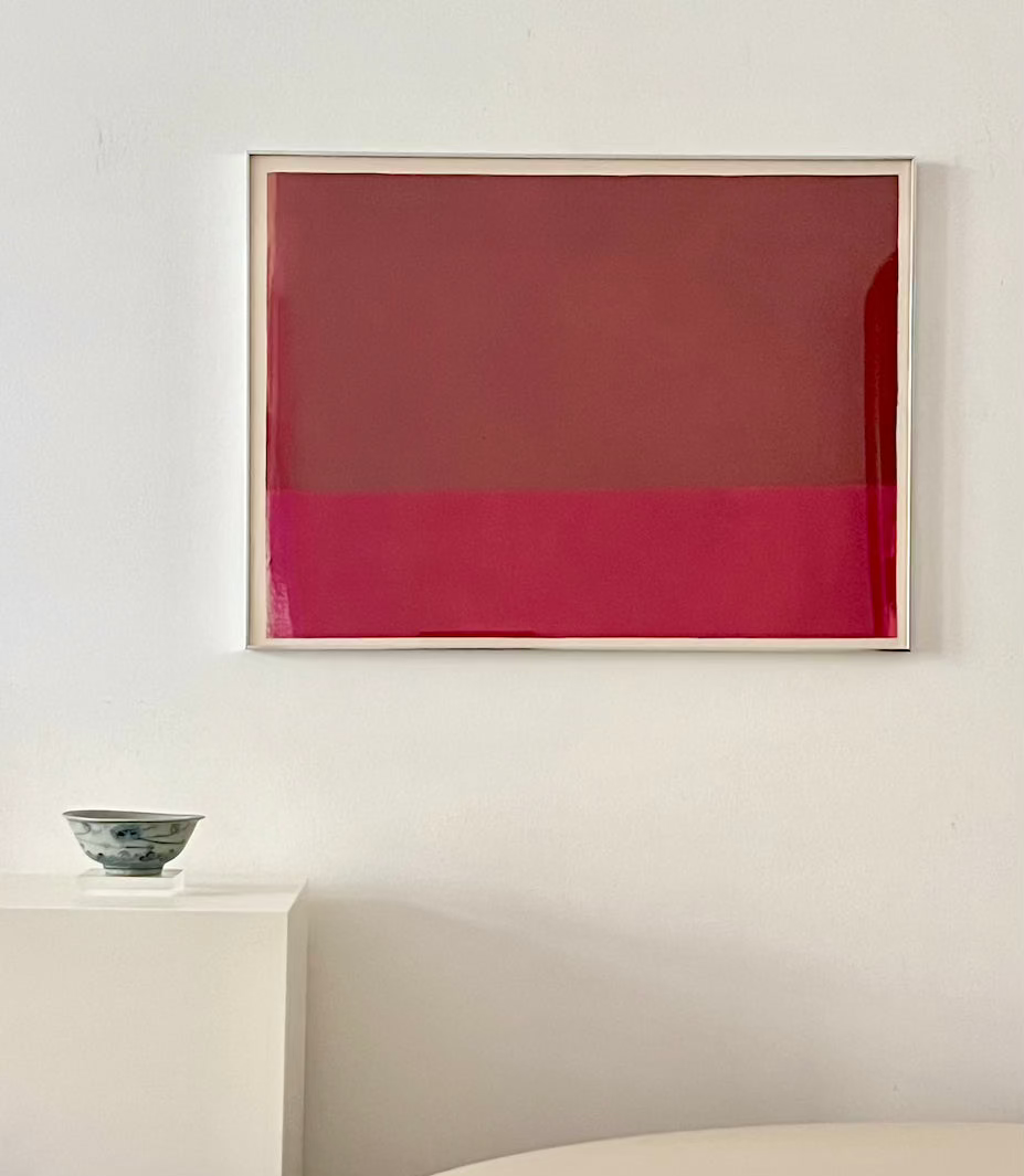 Framed abstract artwork with a red gradient on a white wall above a table.