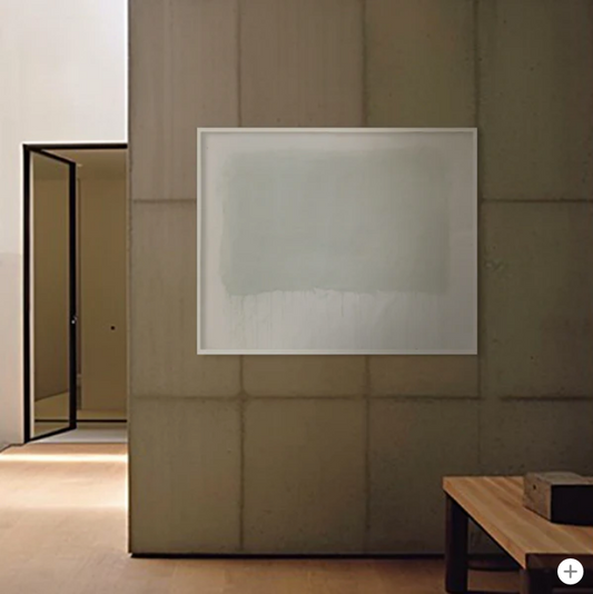 A minimalist artwork displayed on a wall, with a light gray or white rectangular frame, set in a simple room with wooden flooring and a door in the background.