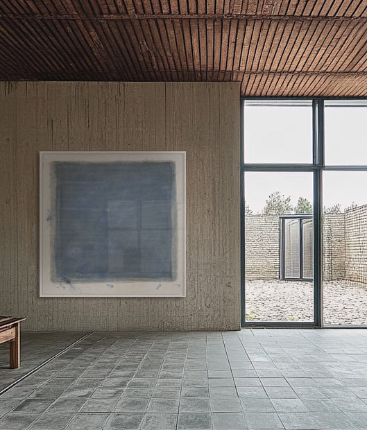 A large abstract artwork in ultramarine color, mounted on a wall in a room with a wooden frame, second artwork in background.