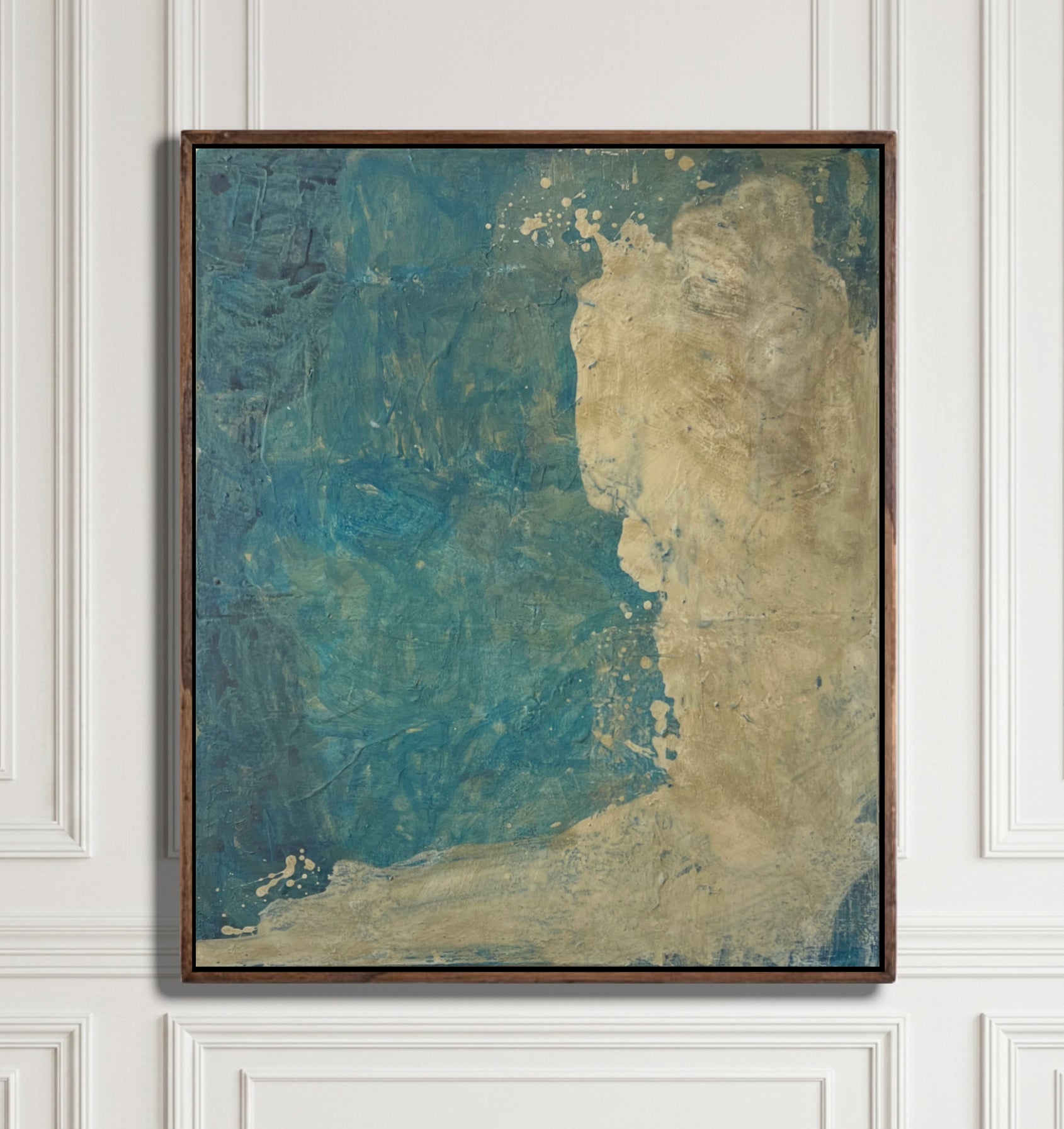 An abstract framed painting featuring textured blue and beige tones, hung on a white paneled wall.
