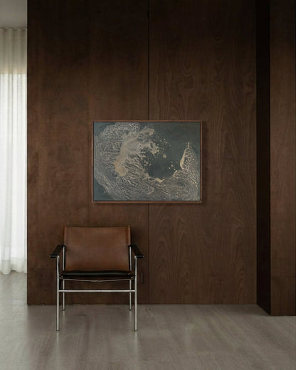 A modern interior scene featuring a dark brown wood-paneled wall with a framed abstract landscape print and a brown leather chair with chrome legs, set in a minimalist room with light wood floors and a sheer white curtain.