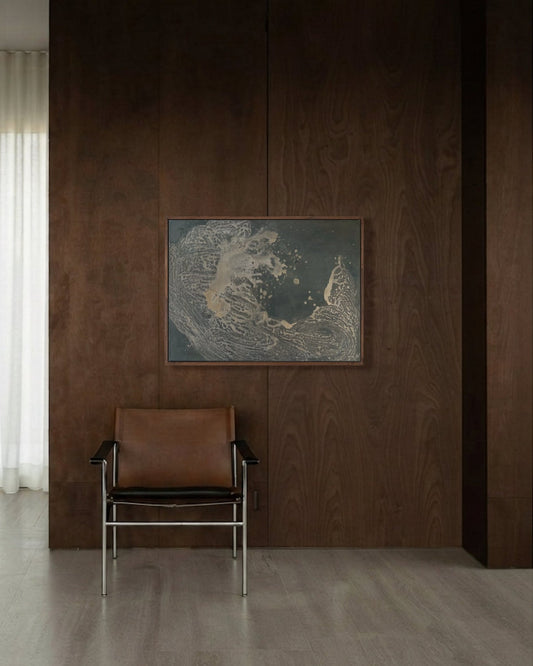 A modern interior scene featuring a dark brown wood-paneled wall with a framed abstract landscape print and a brown leather chair with chrome legs, set in a minimalist room with light wood floors and a sheer white curtain.