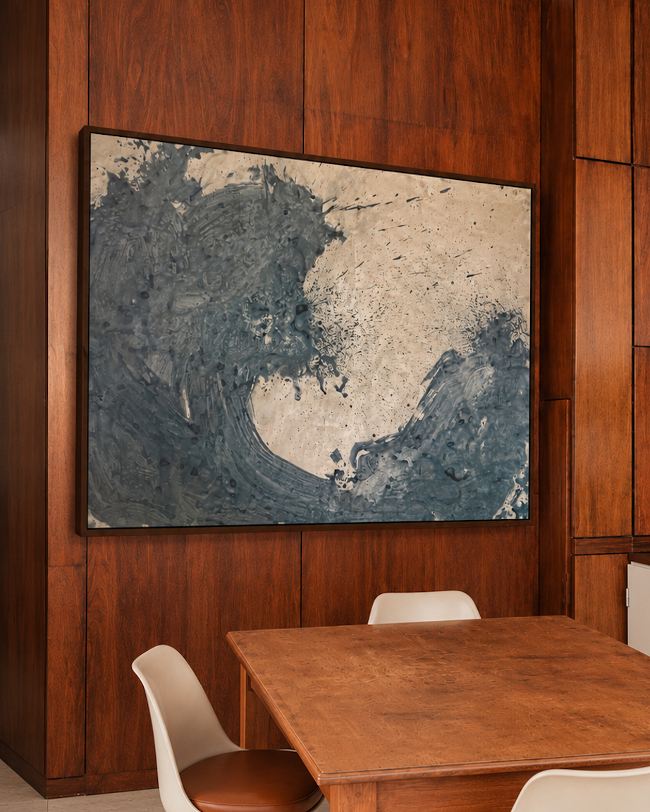 A large abstract wave painting in blue, gray by Nicolas Makelberge, and beige hangs on a dark wood-paneled wall above a wooden dining table with white chairs in a modern dining room.
