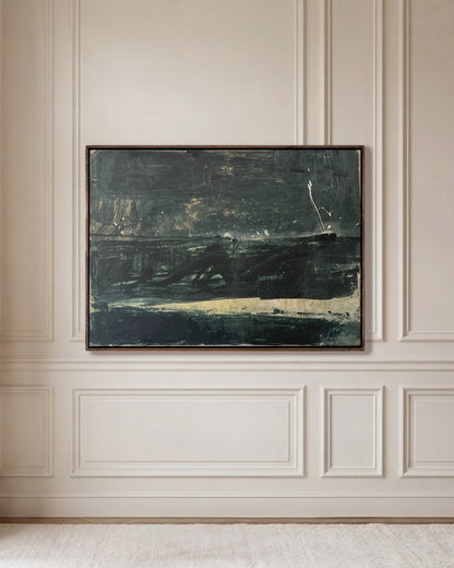 An abstract landscape painting in dark green, black, and beige tones, framed in a dark wood frame and hung on a cream paneled wall in a bright, modern room.