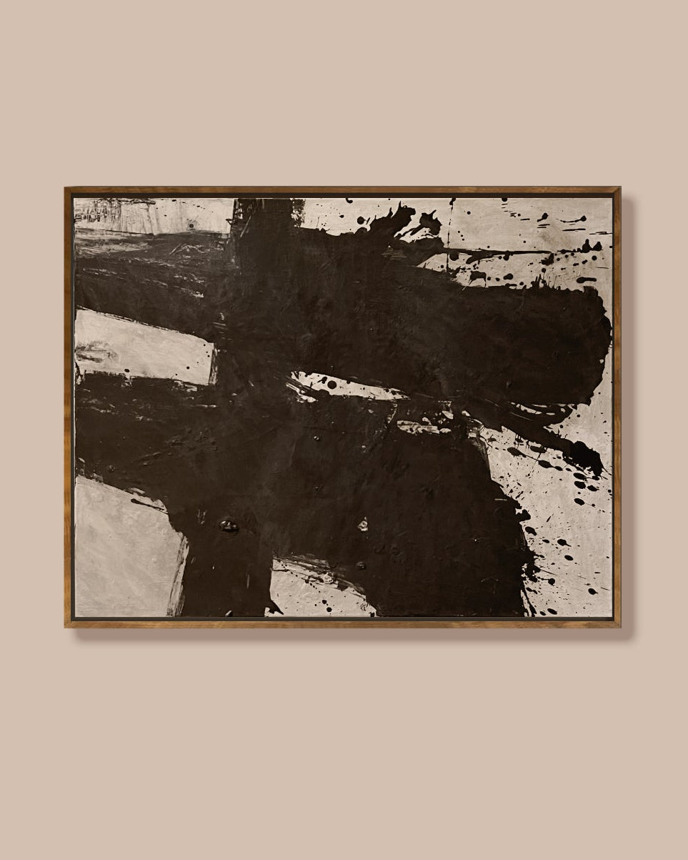 An abstract black and white painting with thick brushstrokes by Nicolas Makelberge, framed in a thin brown wooden frame and displayed on a beige wall.