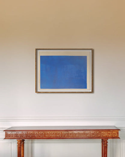 Framed blue abstract painting on a white wall above a wooden mantelpiece.