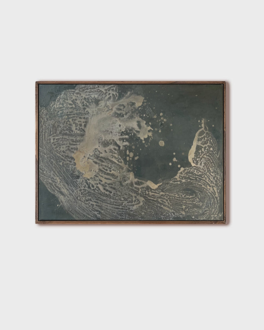 A framed abstract art print featuring textured organic patterns in dark gray, beige, and gold tones, set against a solid light gray background.